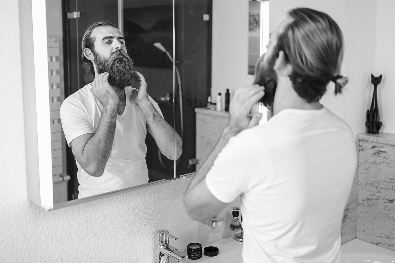 Mann betrachtet seinen Bart im Spiegel.