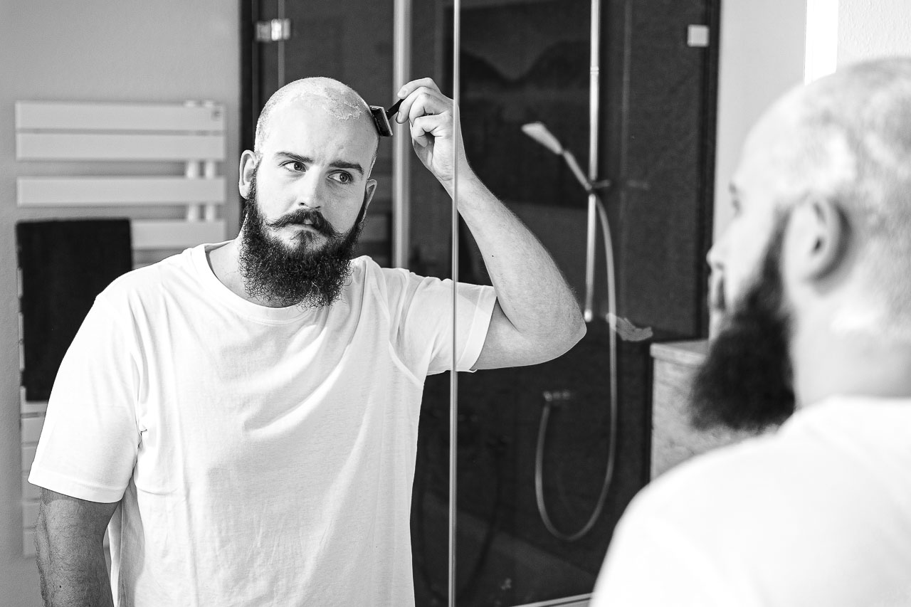 Mann mit Vollbart, rasiert sich seine Glatze, mit einem Rasierhobel.