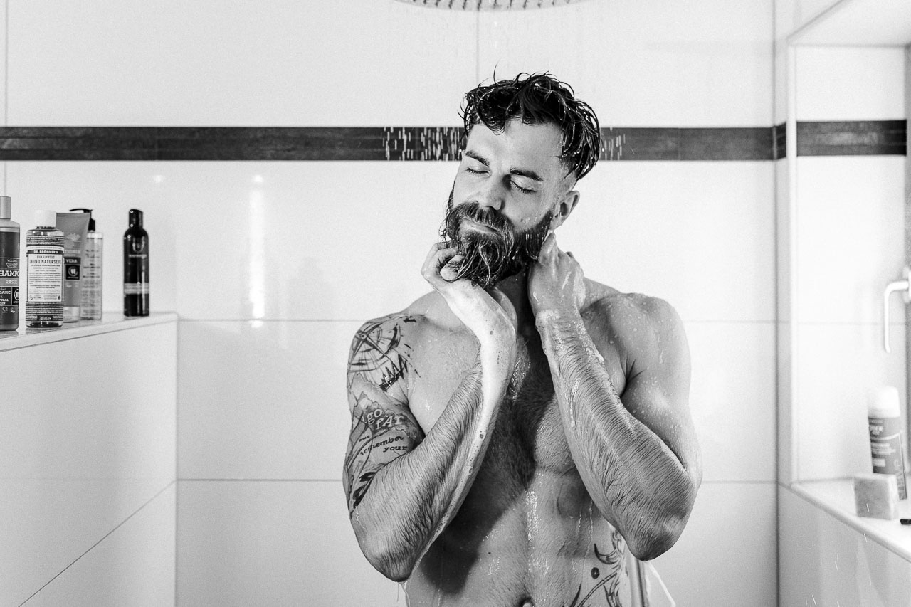 Mann mit Bart duscht sich.