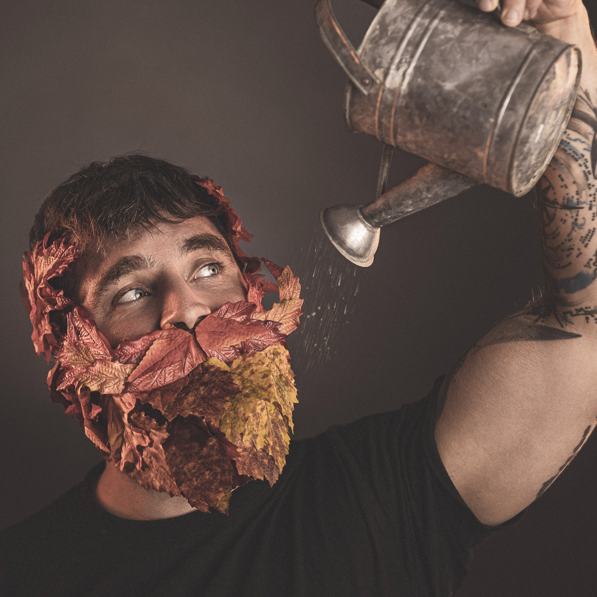Ein Mann mit einem Bart aus Laubblättern gießt seinen Bart mit Wasser aus einer Gießkanne.