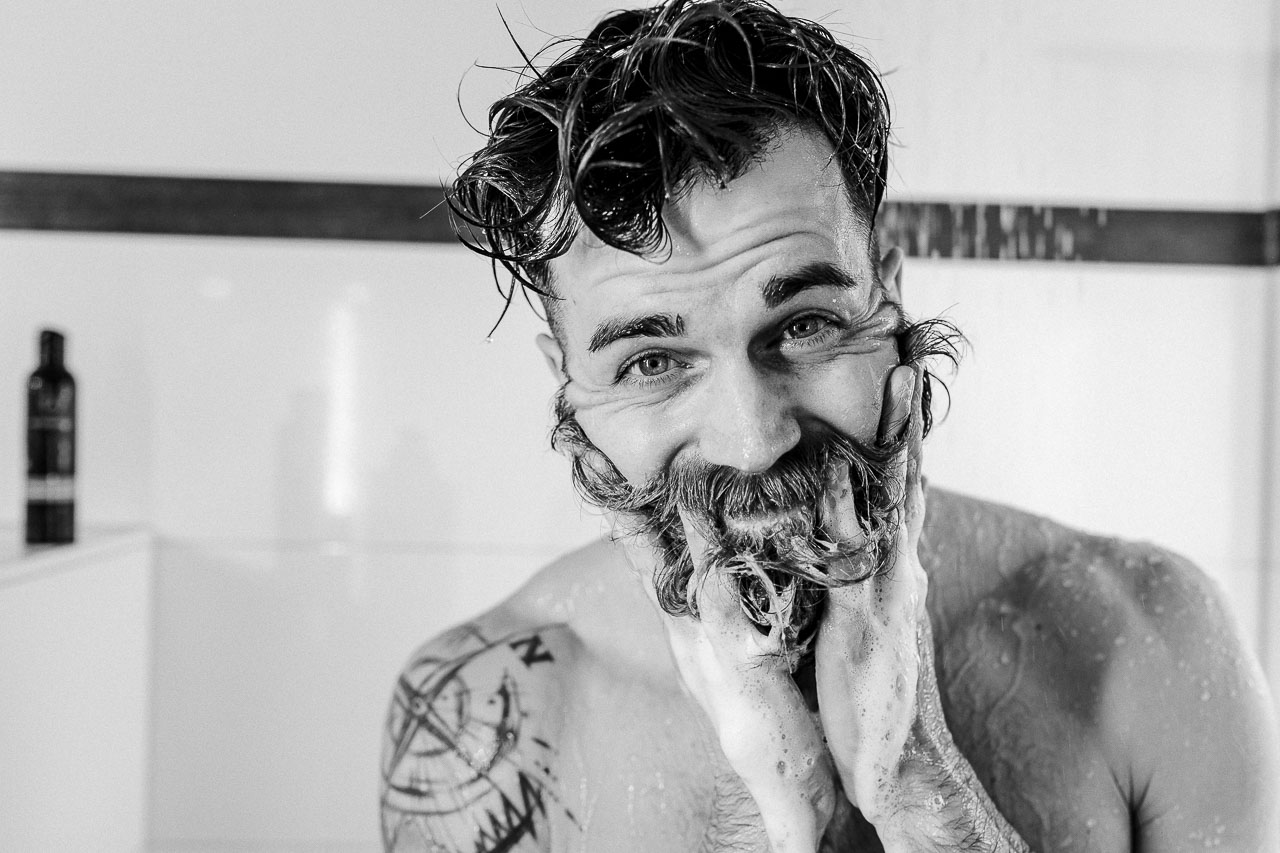Mann schäumt seinen Bart unter der Dusche mit Bartshampoo ein.