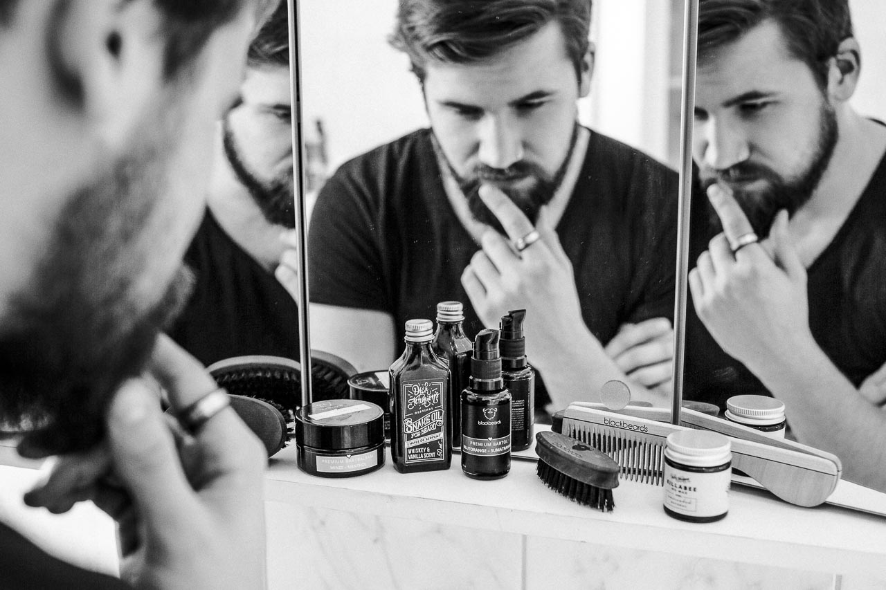 Mann schaut skeptisch auf diverse Bartpflege Produkte.