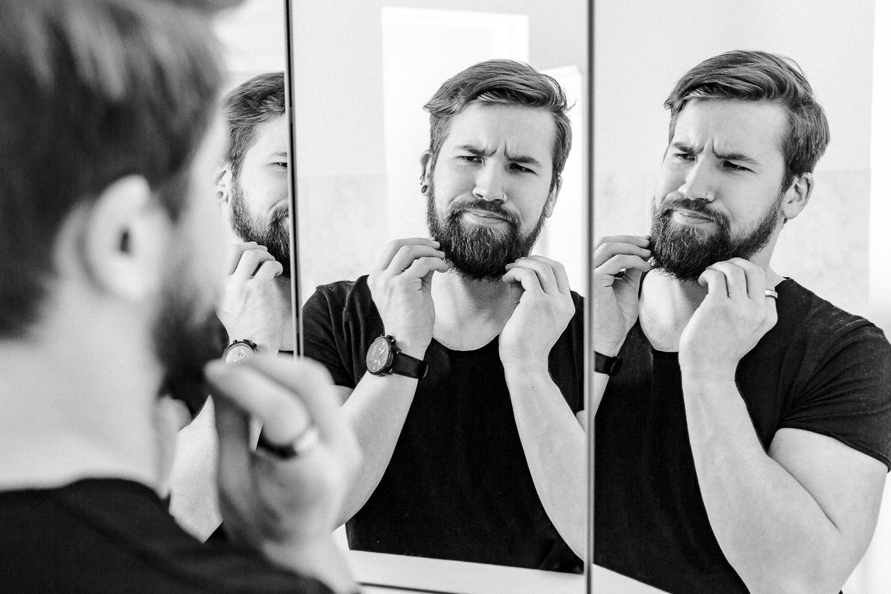 Mann mit Bart schaut skeptisch in den Spiegel.