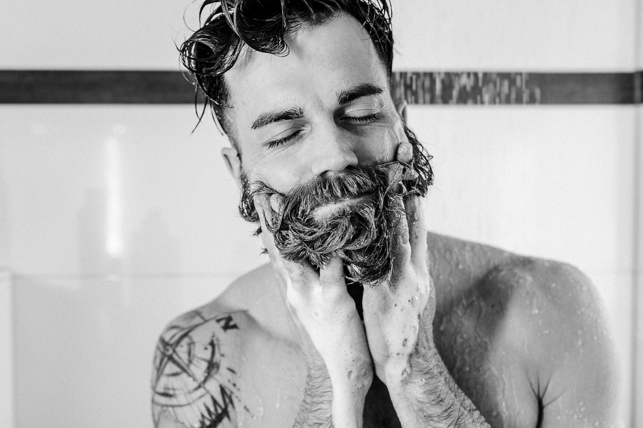 Mann schäumt sich unter der Dusche seinen Bart ein.