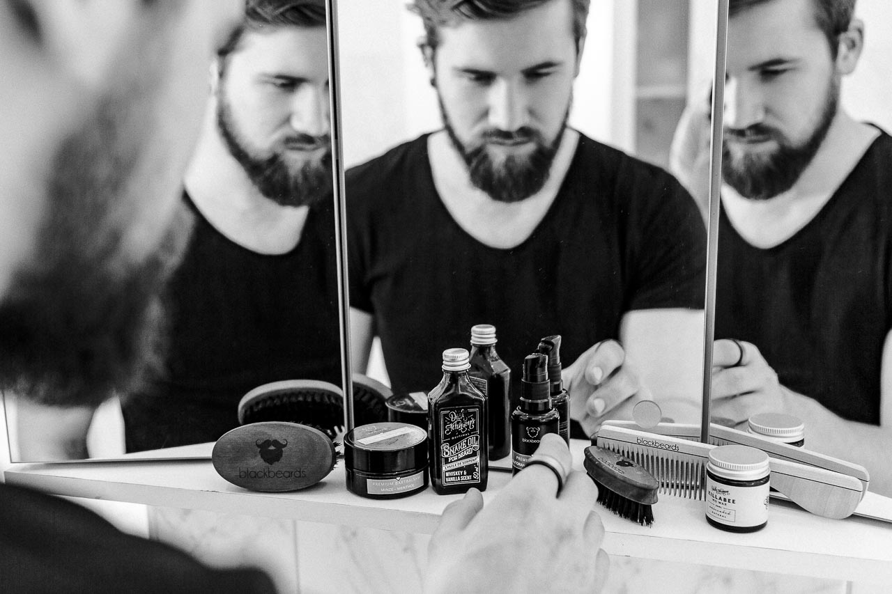 Mann mit Bart schaut sich verschiedene Bartpflege-Produkte an.