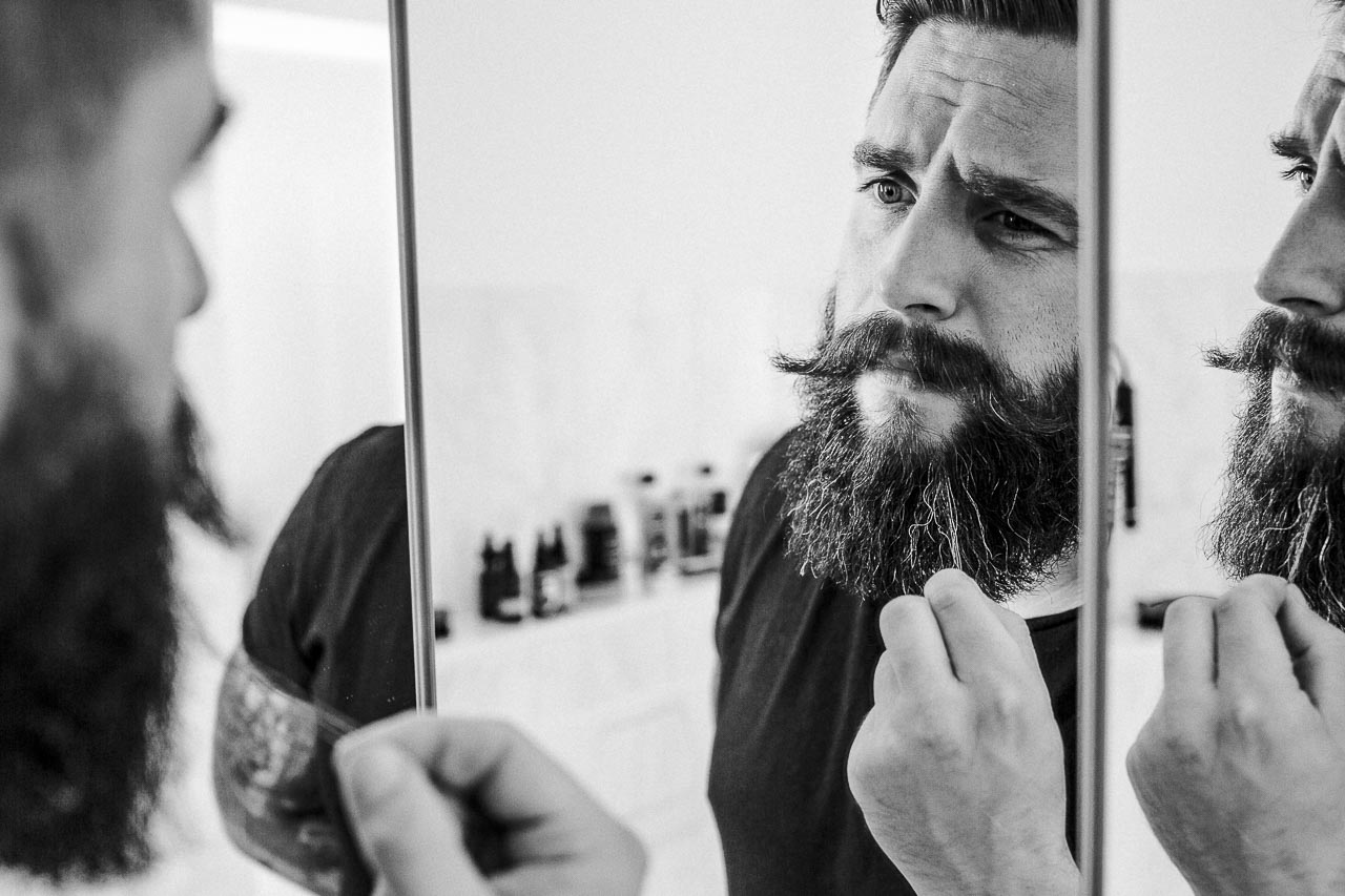 Mann mit Bart schaut fragend in den Spiegel.